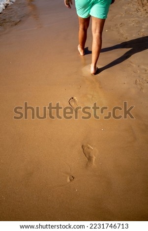 Man walking along the shore of the Levante beach in Benidorm in a swimsuit leaving his footprints in the fine sand behind him.

