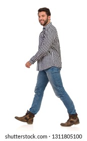 Man is walking in boots, jeans and lumberjack shirt, smiling and looking at camera. Side view. Full length studio shot isolated on white.