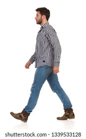 Man is walking in boots, jeans and lumberjack shirt and looking away. Side view. Full length studio shot isolated on white.