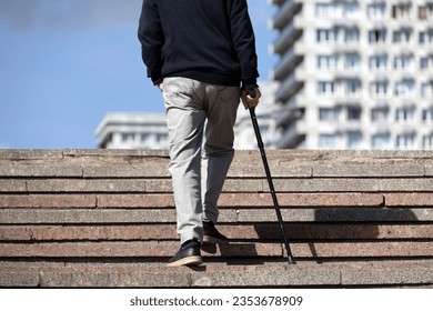 Man with walking cane climbing stairs on city street. Concept for disability, limping adult
