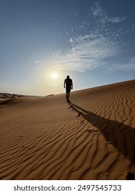 Man walking in desert, while the sky is clear and it's all long desert land. A silhouette of a man walking in the sand. Clear sky with sun. 