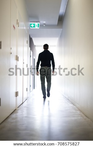 Man walking down a corridor towards a well lit endexit doctor from behind light bright walk 