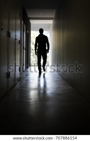 Man walking down a dark corridor towards a well lit end/exit