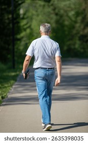 A man is walking down a path with a blue shirt and jeans. He is carrying a black purse and a book