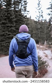 Man Walking Down a Path in the Woods - A person is seen walking down a narrow path surrounded by dense trees and foliage in a forest setting. The individual is moving steadily forward on the trail
