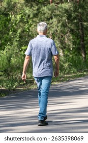 A man is walking down a path in the woods. He is wearing a blue shirt and blue jeans