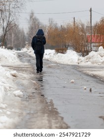 A man is walking down a snowy road with a backpack on. The scene is quiet and peaceful, with the snow covering the ground and the man's backpack adding a sense of purpose to his walk