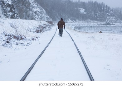 Man walking down a snowy train track.