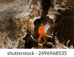 Man walking and exploring dark cave with light headlamp underground.