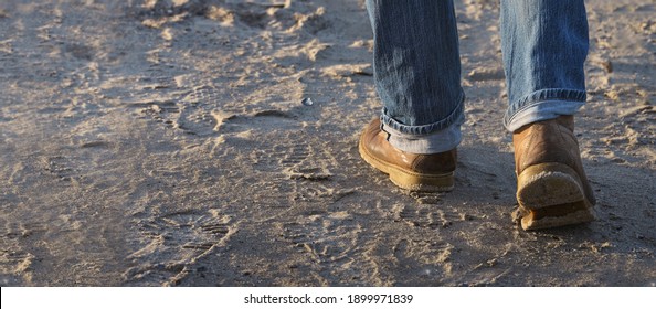 Mann, der sich auf Sand vorwärts bewegt, Füße mit Lederstiefeln und aufgerollte Jeans, Freizeit- oder Arbeitskonzept, selektiver Fokus, schmale Feldtiefe