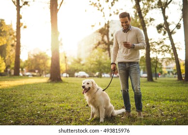 Man Walking His Dog And Texting On A Mobile Phone.