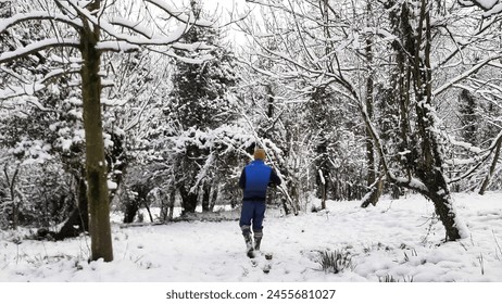 a man is walking into the forest while snowfall.