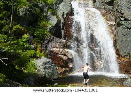 Man walking into the mountains waterfall alone to take a bath there. Travel Lifestyle adventure concept of an active vacations into the wild nature.