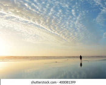 Man walking on beach at sunrise, beautiful cloudy sky reflected on the beach, Jacksonville, Florida, USA. - Powered by Shutterstock