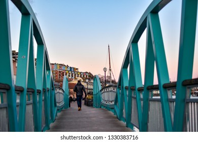 Man walking on Blue / Turquoise footbridge leading from Bristol Harbor towards the well known colorful houses of Clifton -Image