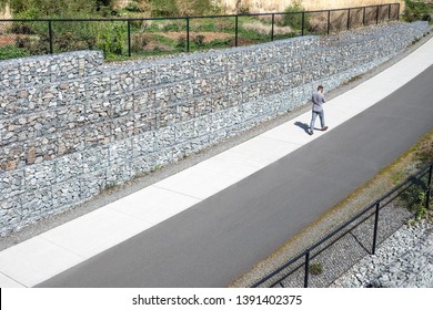 Man walking on a concrete sidewalk along a Gabion stone wall, in a modern transportation background, with space for text on the left