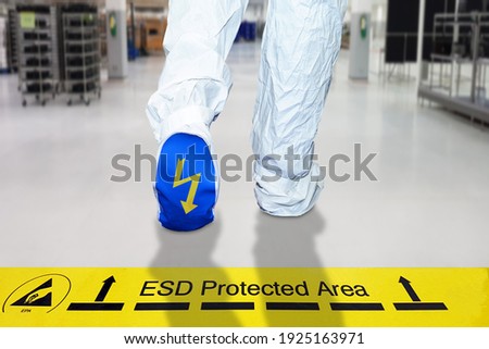 Man walking on a electrostatic control floor and cleanliness control suit with ESD symbol on the foot,  A yellow tape with text: "ESD Protected Area" to be careful when entering the ESD area.