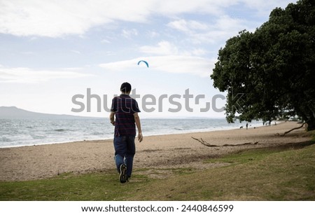 Man walking on Milford Beach. Rangitoto Island in the background. Auckland.