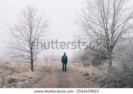 Man walking on path with trees and grass covered frost in morning fog. Czech winter landscape
