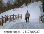 A man is walking on a snowy path with a backpack. The scene is peaceful and serene, with the snow covering the ground and the man