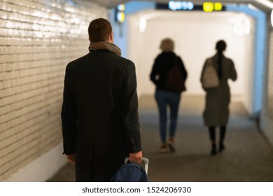 Man walking through a subway pulling a suitcase as he follows two women ahead of him in a concept of travel