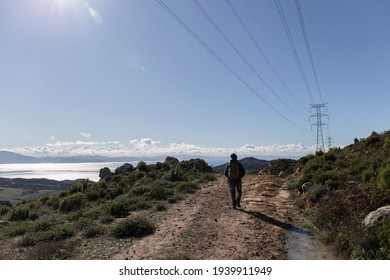 A man walks alone along a country path overlooking the sea, to the right is an electric tower