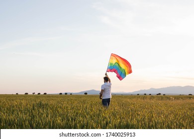 Man Walks Alone Through A Blue Meadow Waving A Rainbow Lgbt Flag. Concept Of Sadness For The Suspension Of Gay Pride Events 2020