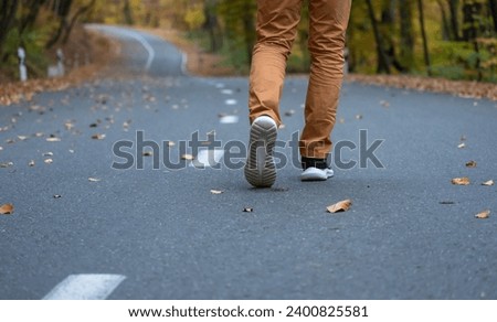 A man walks along an asphalt road in autumn

