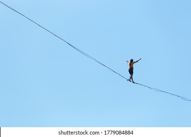 A man walks along the highline against the blue sky. Highliner goes on a stretched sling. Tightrope walker. A man catches balance. - Shutterstock ID 1779084884
