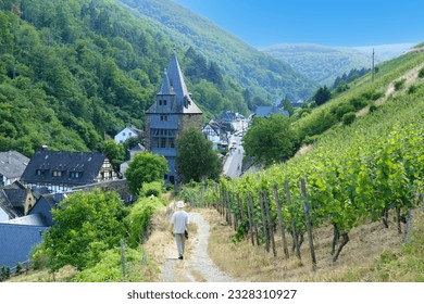 man walks along narrow road in gorge among old houses, watchtowers and vineyards in Middle Rhine valley above town of Bacharach in Mainz-Bingen district in Rhineland-Palatinate, medieval charm