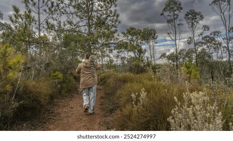 A man walks along a red soil dirt path. A ring-tailed lemur catta sits on his shoulder. Another lemur is standing on the ground. Thickets of grass, bushes, and trees on the roadsides. Madagascar.   - Powered by Shutterstock