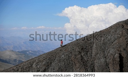 A man walks down a steep slope against a backdrop of incredible thick clouds and summer haze