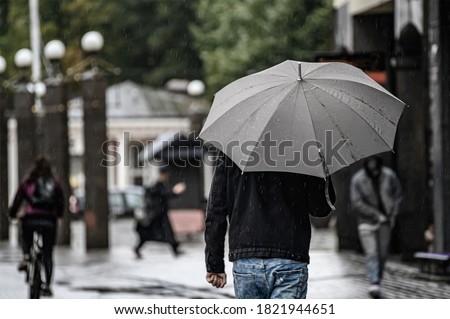 A man walks down the street under a gray umbrella. Rain in early autumn.