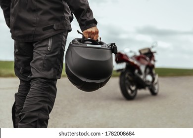 A man walks to his motorcycle, holding a helmet in his hands. Motorcycle helmet close up - Shutterstock ID 1782008684