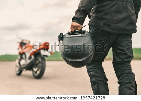 A man walks to his motorcycle, holding a helmet in his left hand. Motorcycle helmet close up