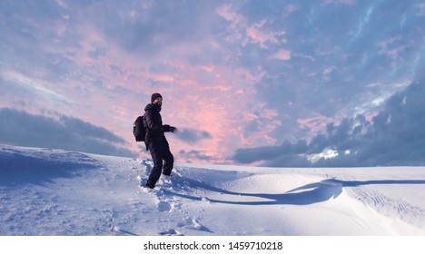 A man walks on the first snow, goes uphill in the snow against a dramatic winter sunset - Powered by Shutterstock