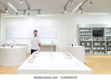 Man Walks On A Light Modern Technology Store. Choosing Gadgets In The Electronics Store. A Modern Tech Shop With A Stylish Light Interior