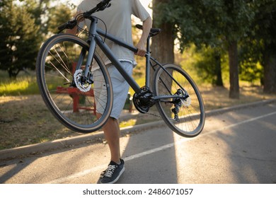 man walks on a paved path in a park, carrying a black bicycle over his shoulder - Powered by Shutterstock