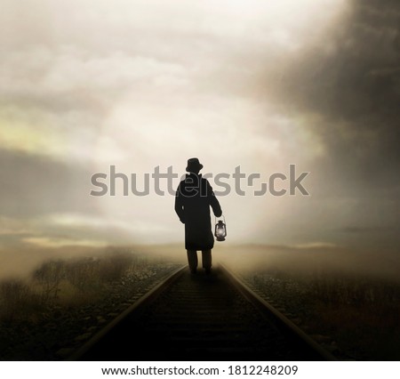 man walks on the rail road with a lantern following the light that comes from afar