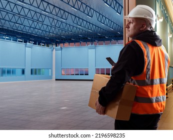 Man Warehouse Worker. Empty Warehouse. A Worker In An Orange Vest Carries A Box