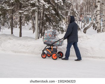 A Man In Warm Clothes, A Father Or Grandfather Walking In The Winter Park With A Baby Carriage, The Concept Of A Happy Family And Caring Parents