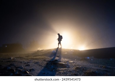 A man in warm yellow backlight and haze with large rocks in the foreground and a long shadow is positioned in the center of the frame. horizontal photo - Powered by Shutterstock