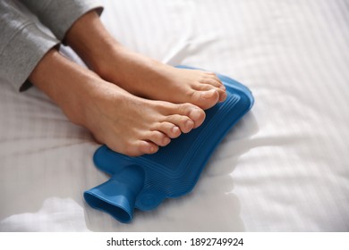 Man Warming Feet With Hot Water Bottle On Bed, Closeup