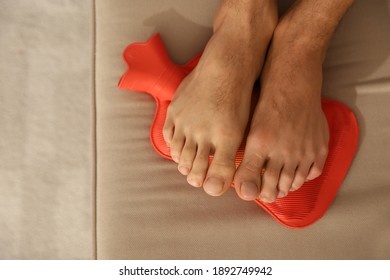 Man Warming Feet With Hot Water Bottle On Sofa, Closeup