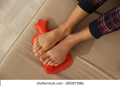 Man Warming Feet With Hot Water Bottle On Sofa, Closeup