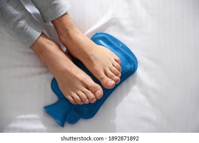 Man Warming Feet With Hot Water Bottle On Bed, Closeup