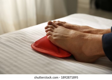 Man Warming Feet With Hot Water Bottle On Bed, Closeup