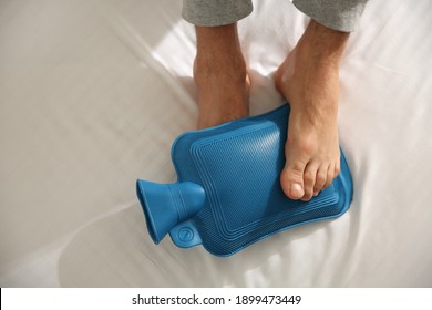 Man Warming Feet With Hot Water Bottle On Bed, Closeup