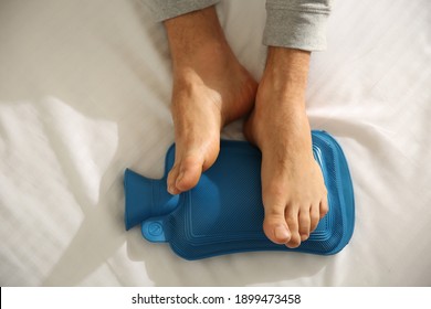 Man Warming Feet With Hot Water Bottle On Bed, Closeup