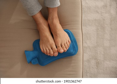 Man Warming Feet With Hot Water Bottle On Sofa, Closeup